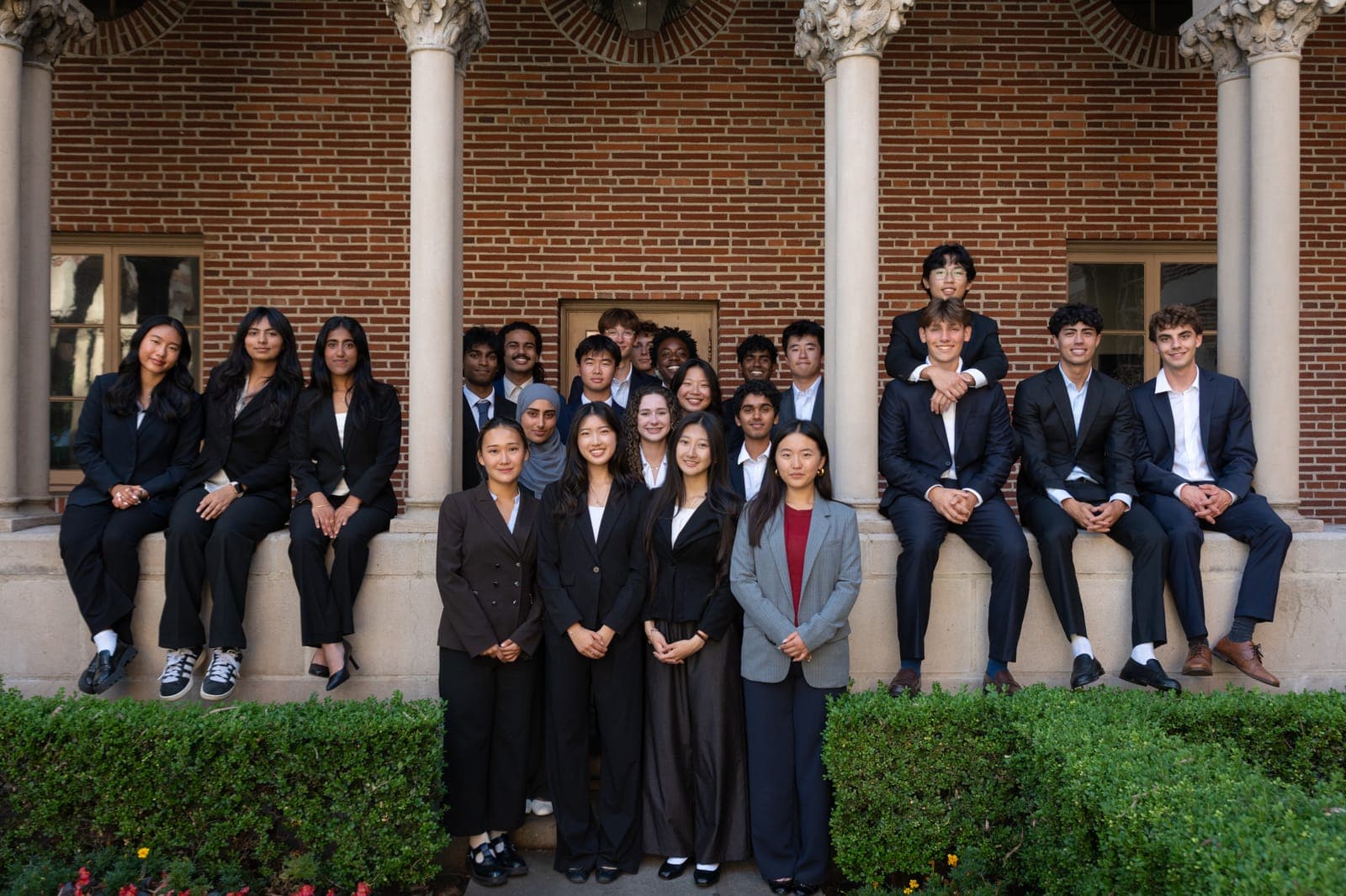 The 180 Degrees Consulting chapter at USC: around two dozen students in business attire gathered on a ledge outside a brick campus building.